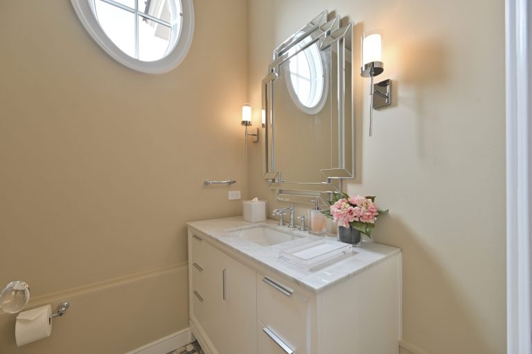 Modern bathroom vanity with marble countertop, geometric mirror, and pink flowers on the sink area