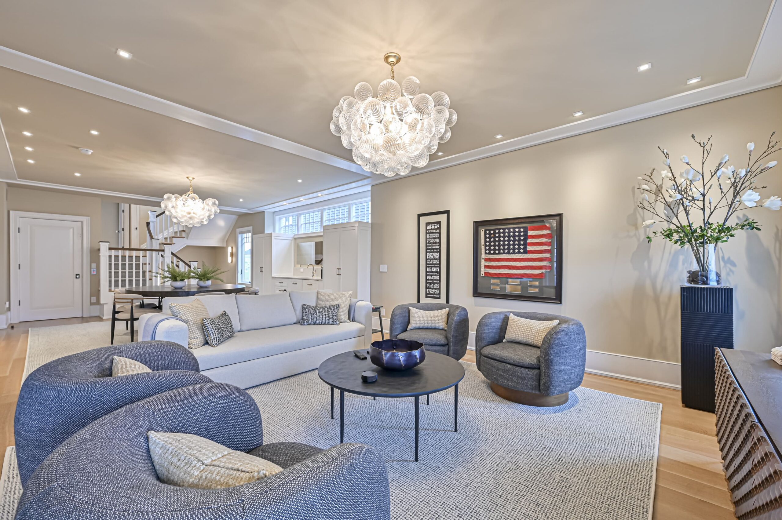 Spacious, modern living room with gray sectional, round coffee table, and a cluster chandelier overhead.