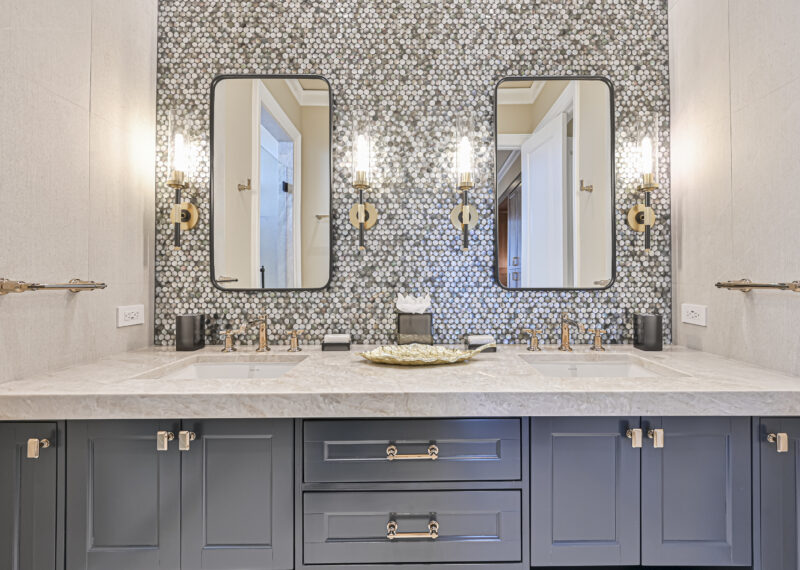 Double sink vanity with navy blue cabinets, gold faucets, and a pebble tile backsplash in a luxurious bathroom.