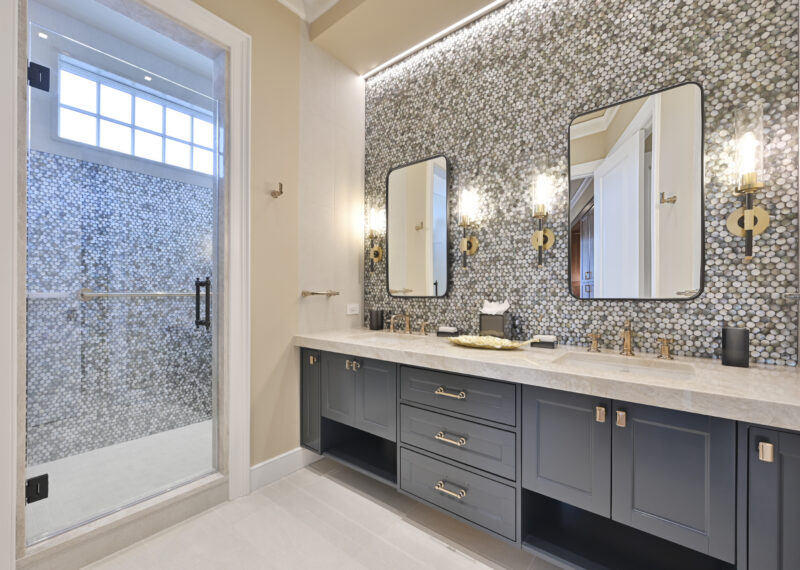 Luxurious bathroom with a dual-sink vanity, pebble mosaic wall, and glass-enclosed shower on the left.