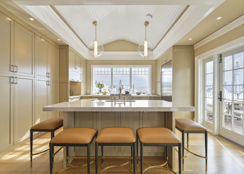 Bright kitchen with cream cabinetry, marble island, and large windows overlooking a neighborhood suburb.