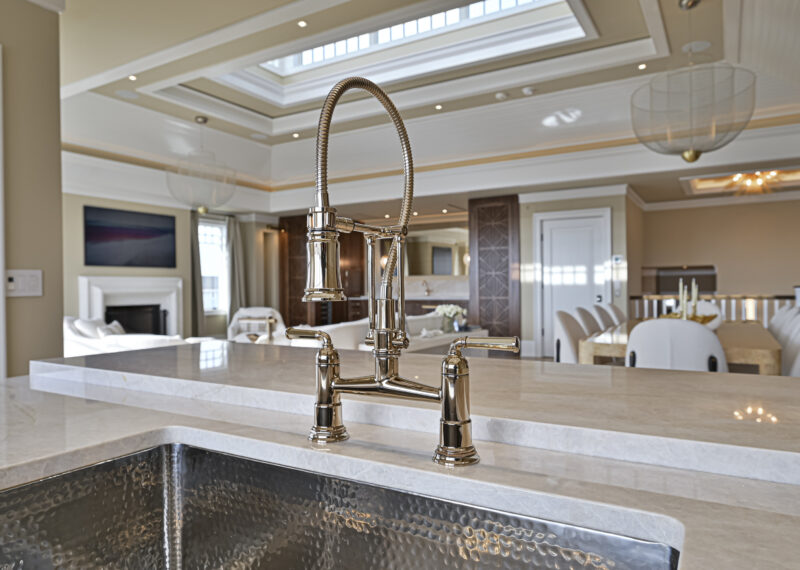 Close-up of a shiny kitchen faucet on a marble island in a bright, modern kitchen