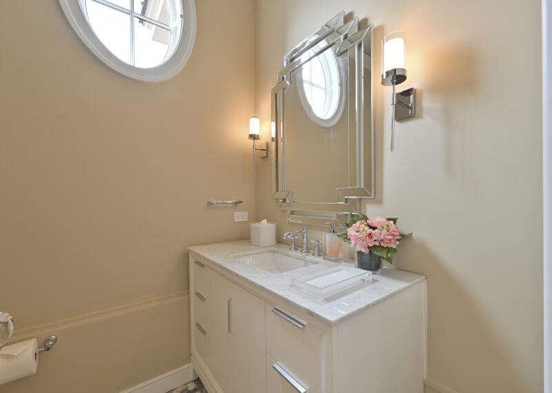 Modern bathroom vanity with marble countertop, round window, and flower arrangement on the sink area